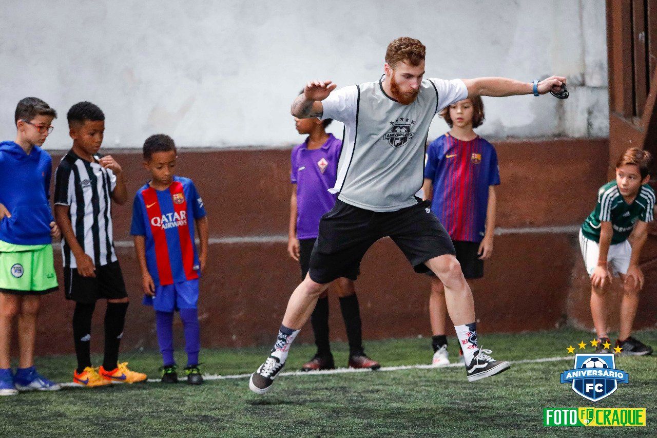 Treinador de futebol demonstrando um salto em frente a um grupo de crianças em um campo.