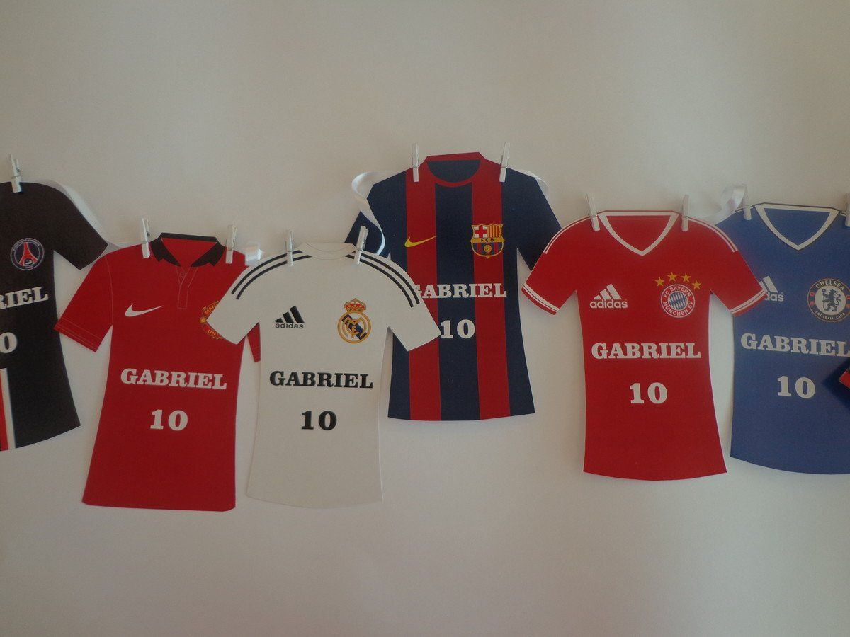 Camisas de futebol de diferentes times, incluindo Paris Saint-Germain e Real Madrid, estão penduradas em uma parede.