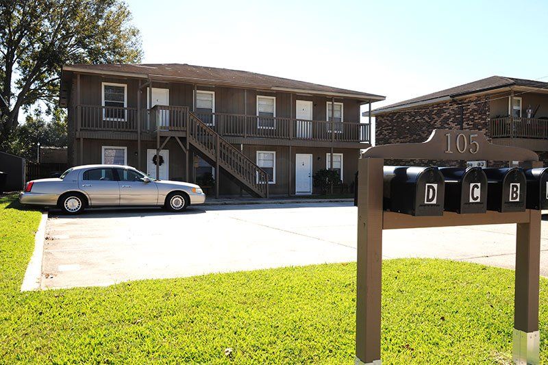 A silver car is parked in front of a brown apartment building.
