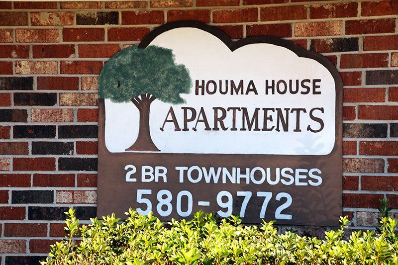 A sign for houma house apartments is on a brick wall