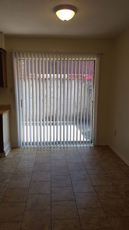 An empty room with a sliding glass door and vertical blinds.