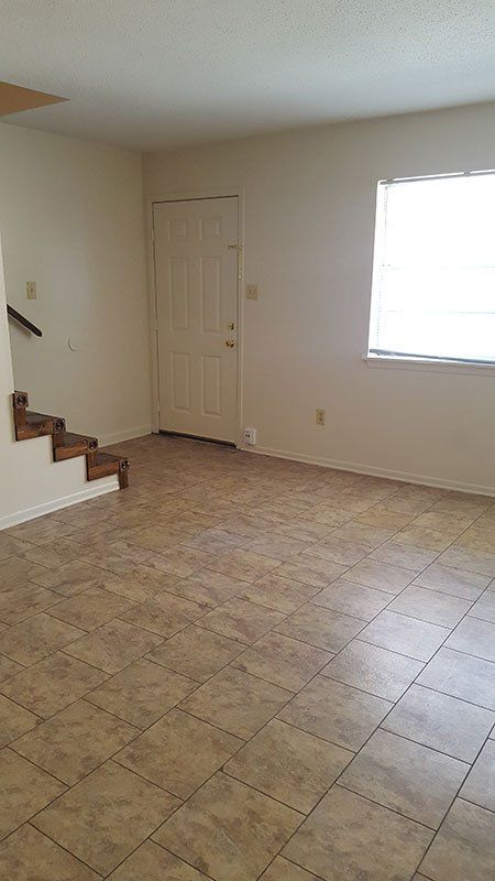 An empty living room with tile floors , stairs and a window.