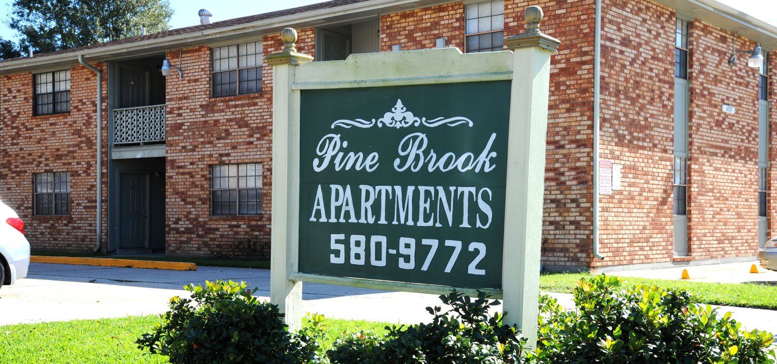 A sign for pine brook apartments is in front of a brick building