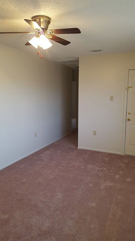 An empty living room with a ceiling fan and a door.