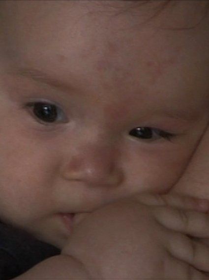 Großaufnahme von einem müden, asiatischen Babygesicht, dass sich an seine Mutter kuschelt.