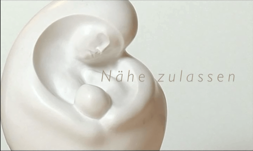 Eine Skulptur aus weißem Marmor die eine stillende Mutter mit ihrem Säugling zeigt. Es ist das Logo des Films Nähe zulassen.