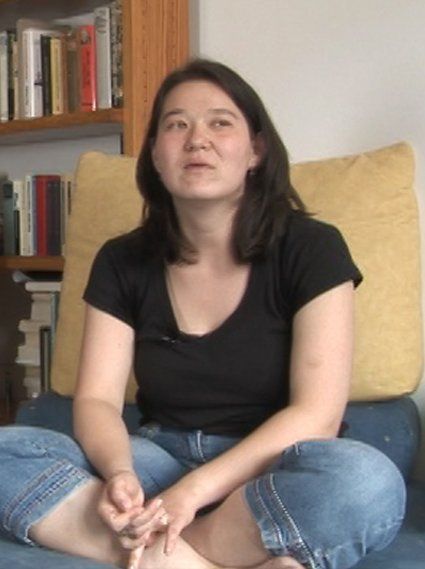 Eine asiatisch anmutende Protagonistin des Films sitzt auf dem Sofa und spricht zur Filmemacherin.