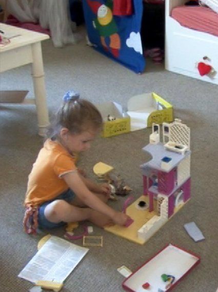 Die 4-jährige Tochter der Protagonisten sitzt auf dem Boden und spielt mit ihrem Puppenhaus – eine Szene aus dem Film.