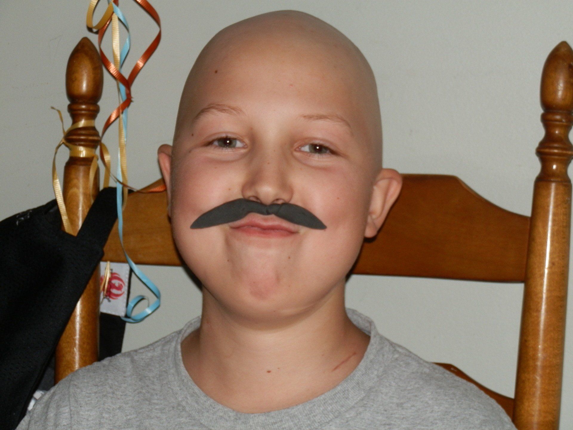 child bald due to chemo wearing fake mustache.