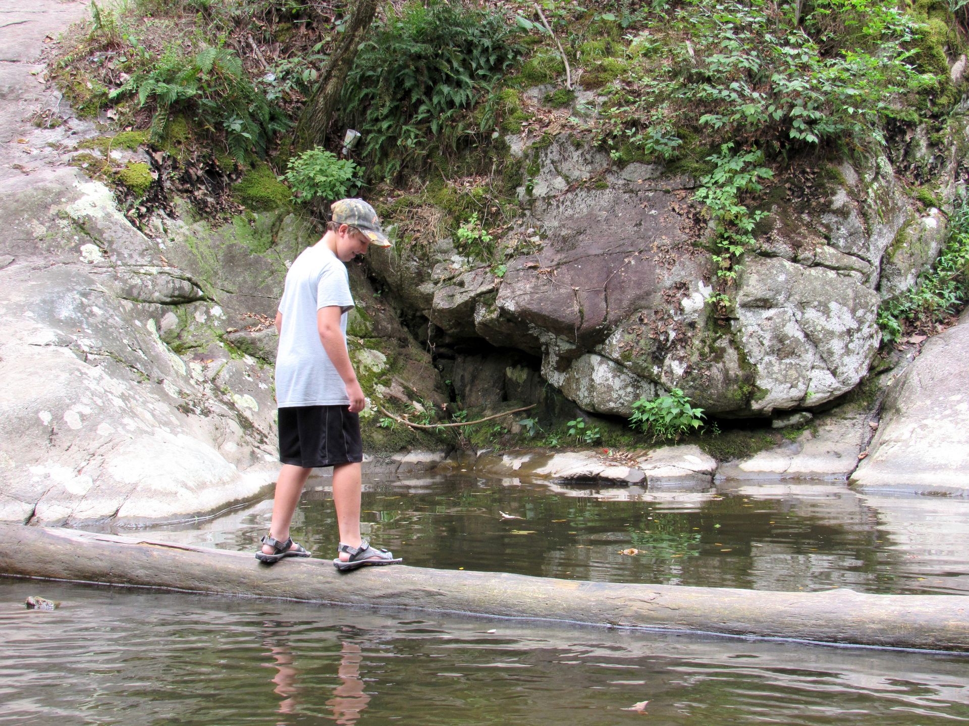 boy standing on a log crossing water.