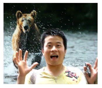 A man in a yellow shirt with the letter t on it stands in front of a bear