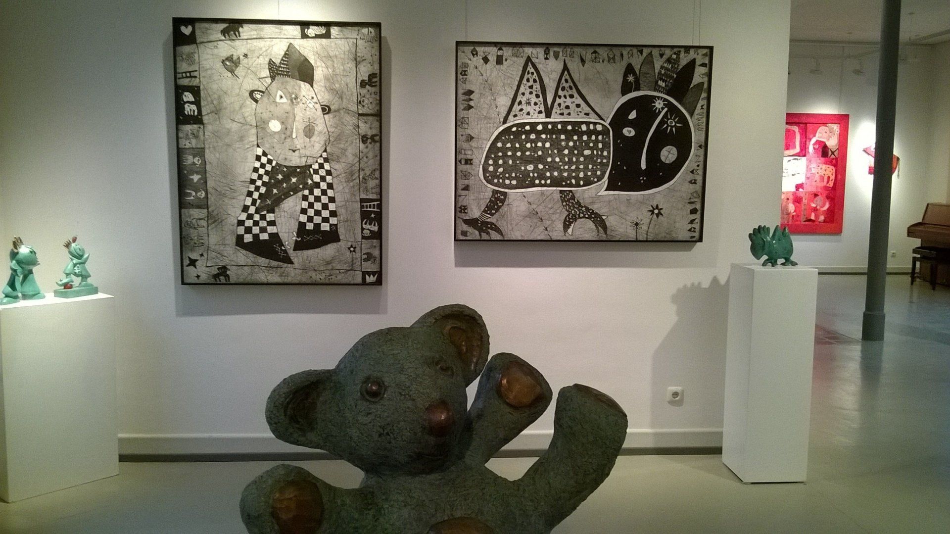 Ein Teddybär sitzt vor einer Wand mit Gemälden darauf
