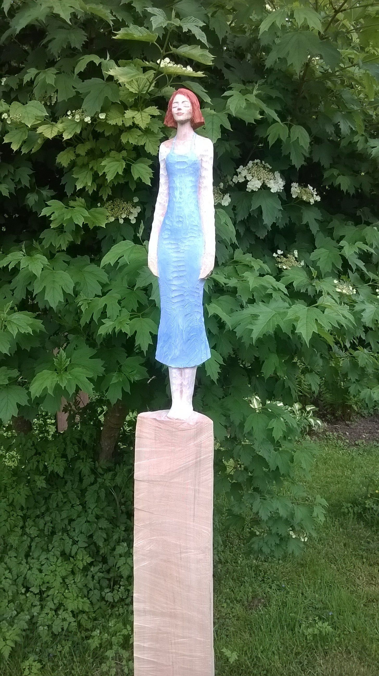 Eine Statue einer Frau in einem blauen Kleid, die auf einem Holzpfosten steht.