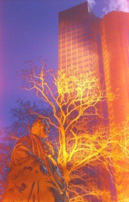 Eine Statue eines Mannes, der neben einem Baum vor einem hohen Gebäude steht.