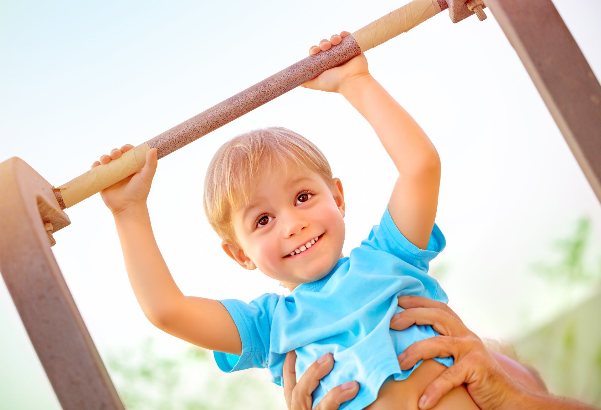 A little boy is hanging on a bar and smiling.