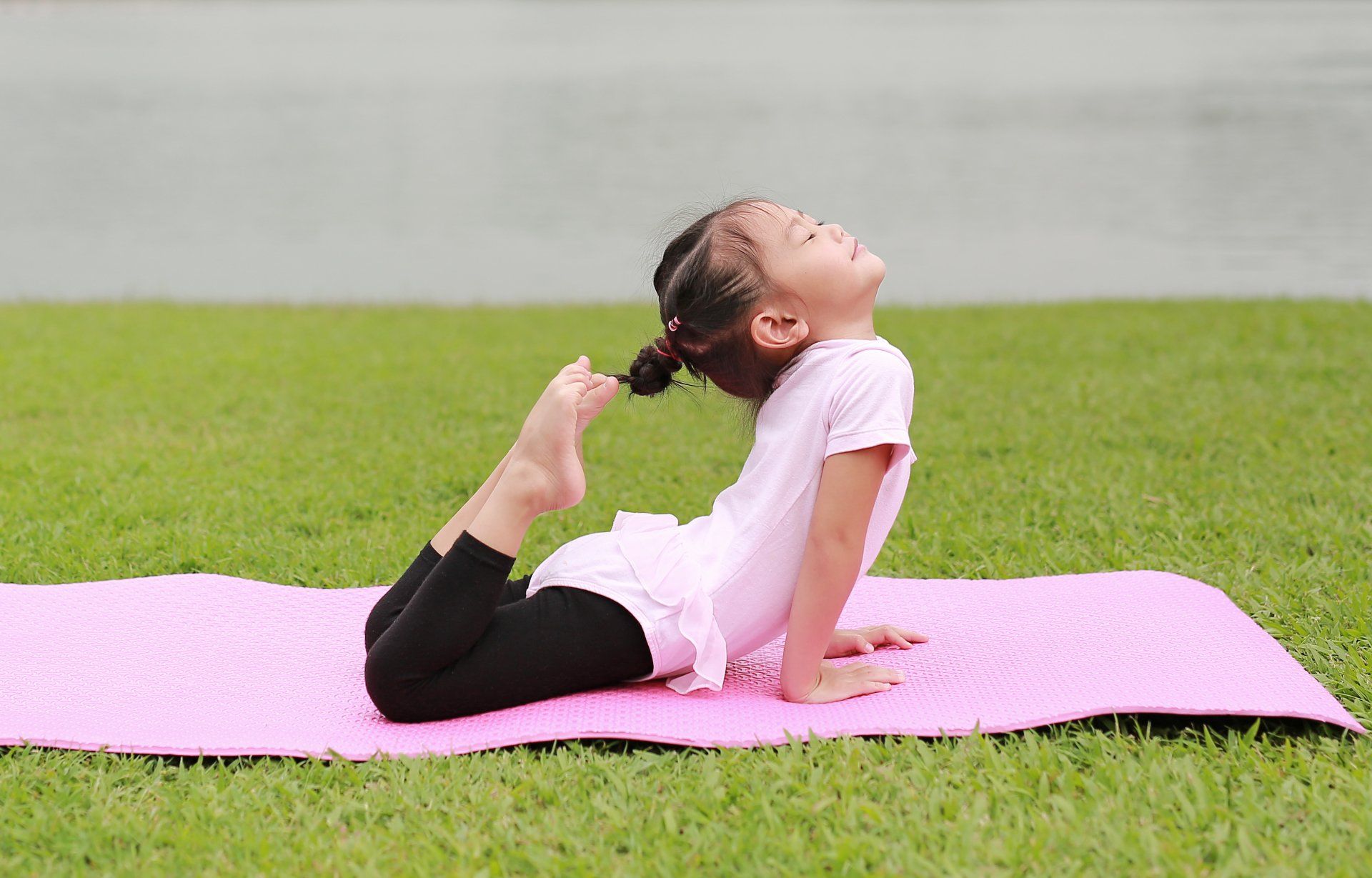 A little girl is laying on a pink yoga mat in the grass.