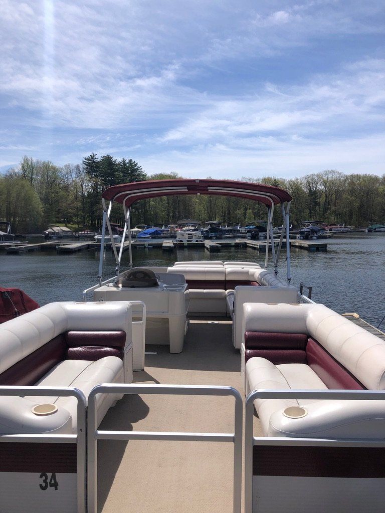 The back of a pontoon boat with red and white seats on a lake.