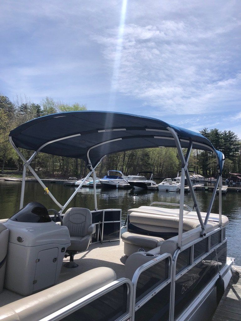 A pontoon boat with a blue canopy is docked at a dock on a lake.