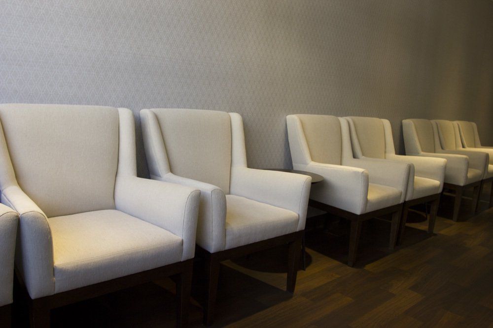 A row of white chairs are lined up in a waiting room.