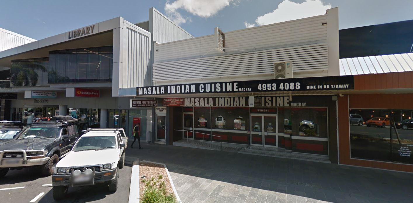 Exterior view of a shopping area, including buildings, parked cars, and a restaurant with the name 