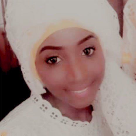 Une femme portant un foulard blanc sourit à la caméra.