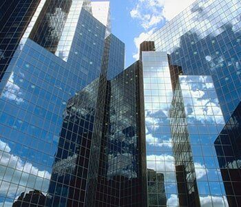 Skyscrapers with glass facades reflect a blue sky with fluffy white clouds.