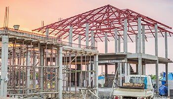 Construction site with concrete frame, red steel roof structure, and a truck.