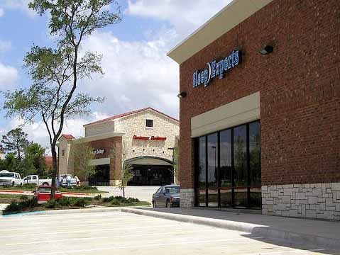 Retail storefronts in a plaza, brick building with Sleep Experts sign.