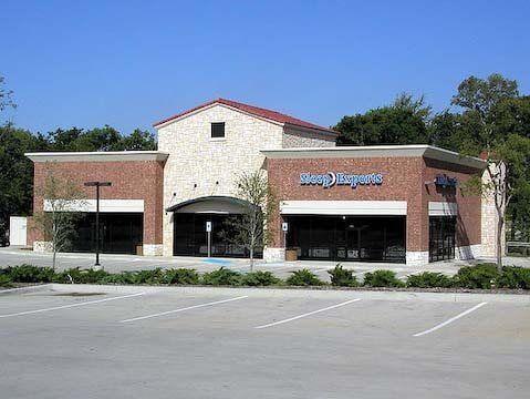 Storefront with Sleep Experts sign; brick and stone exterior, blue sky, empty parking lot.