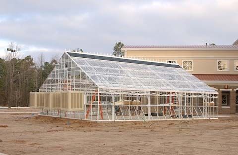 Greenhouse with a white frame and clear panels; next to a building.