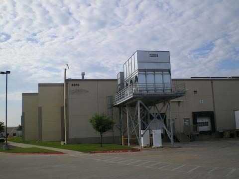 Large industrial building with rooftop machinery on a metal support structure, under a cloudy sky.