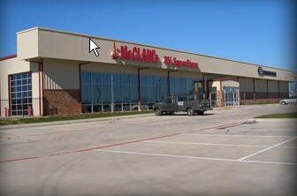McClane's Tire Storefront with glass windows, beige facade, brick accents, a truck parked out front, and blue sky.
