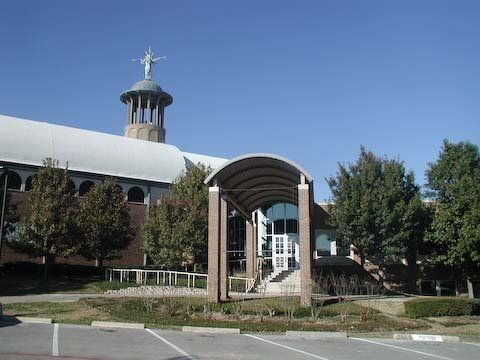 Church building with a central arched entryway, blue sky, and a statue on top.