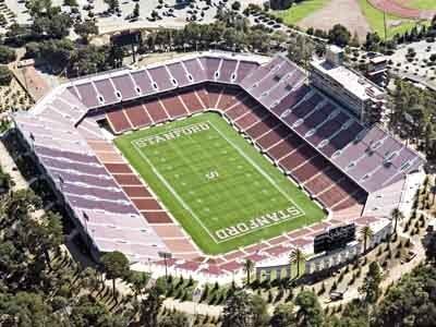 Aerial view of Stanford Stadium; green football field, brown stands, and surrounding trees.