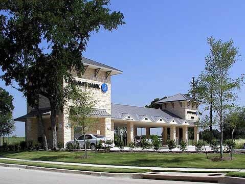 Bank building with stone facade, car in the driveway, trees, and a clear blue sky.