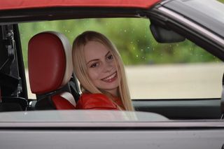 Young lady in drivers seat smiling looking out passenger window.