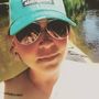 A woman wearing a blue hat and sunglasses is taking a selfie
