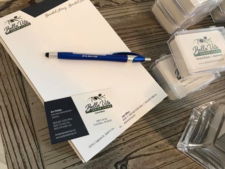 Business stationery set with white notepad, blue pen, cards, and branded coasters on a wooden table