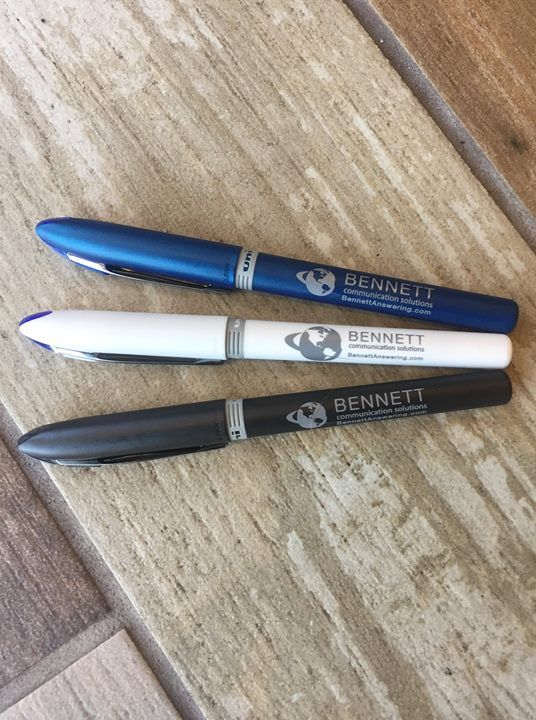 Three Bennett pens in blue, white, and black on a wooden surface.