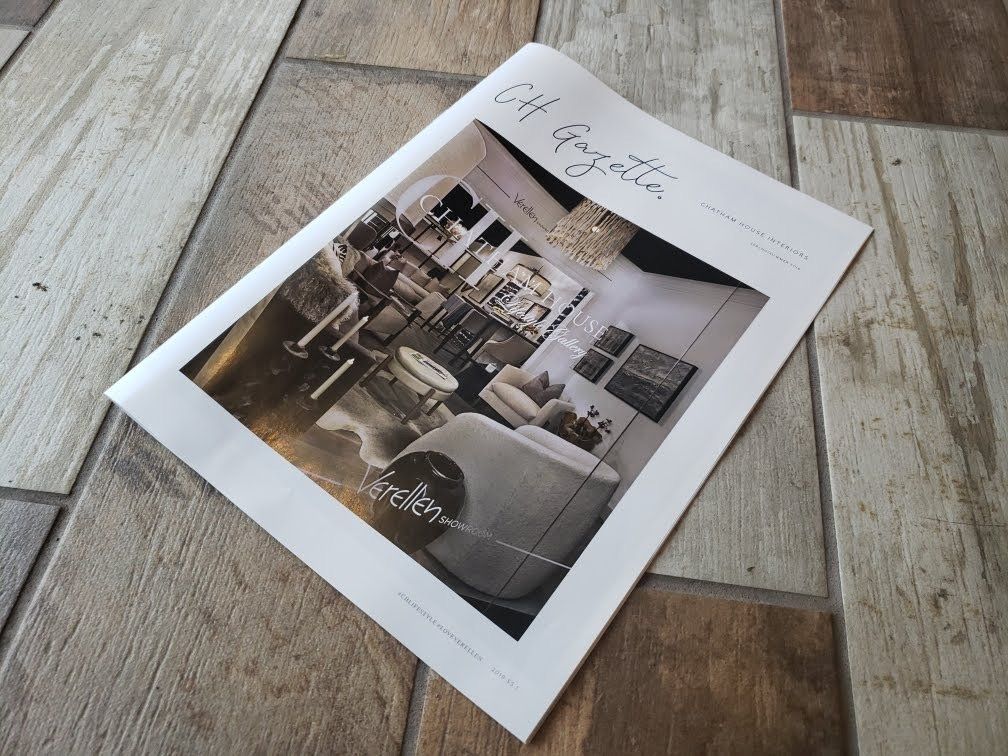 A white brochure on gray wood planks, showing a black-and-white interior photo on the cover.