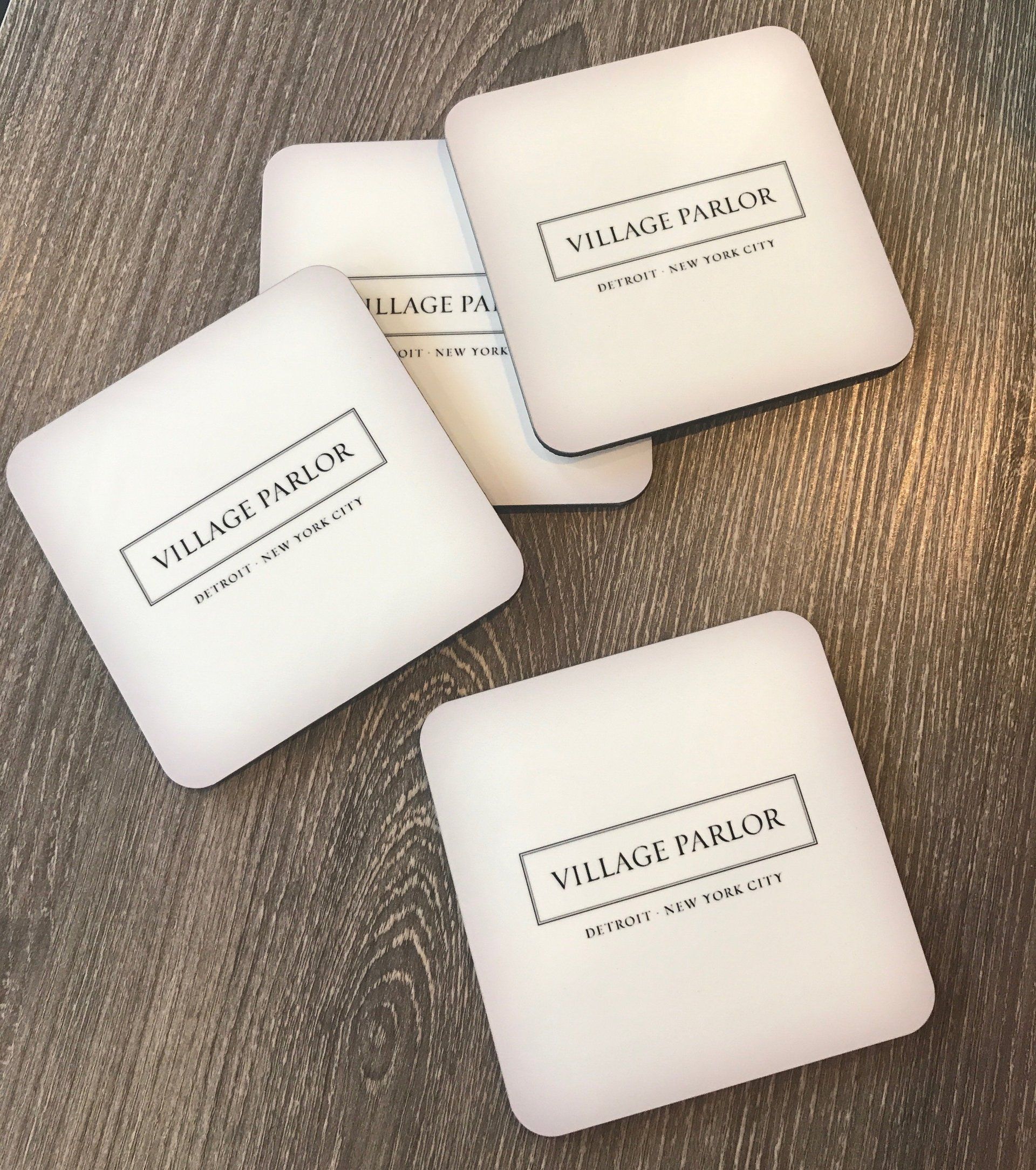 Four white square coasters with black logos on a textured brown surface.