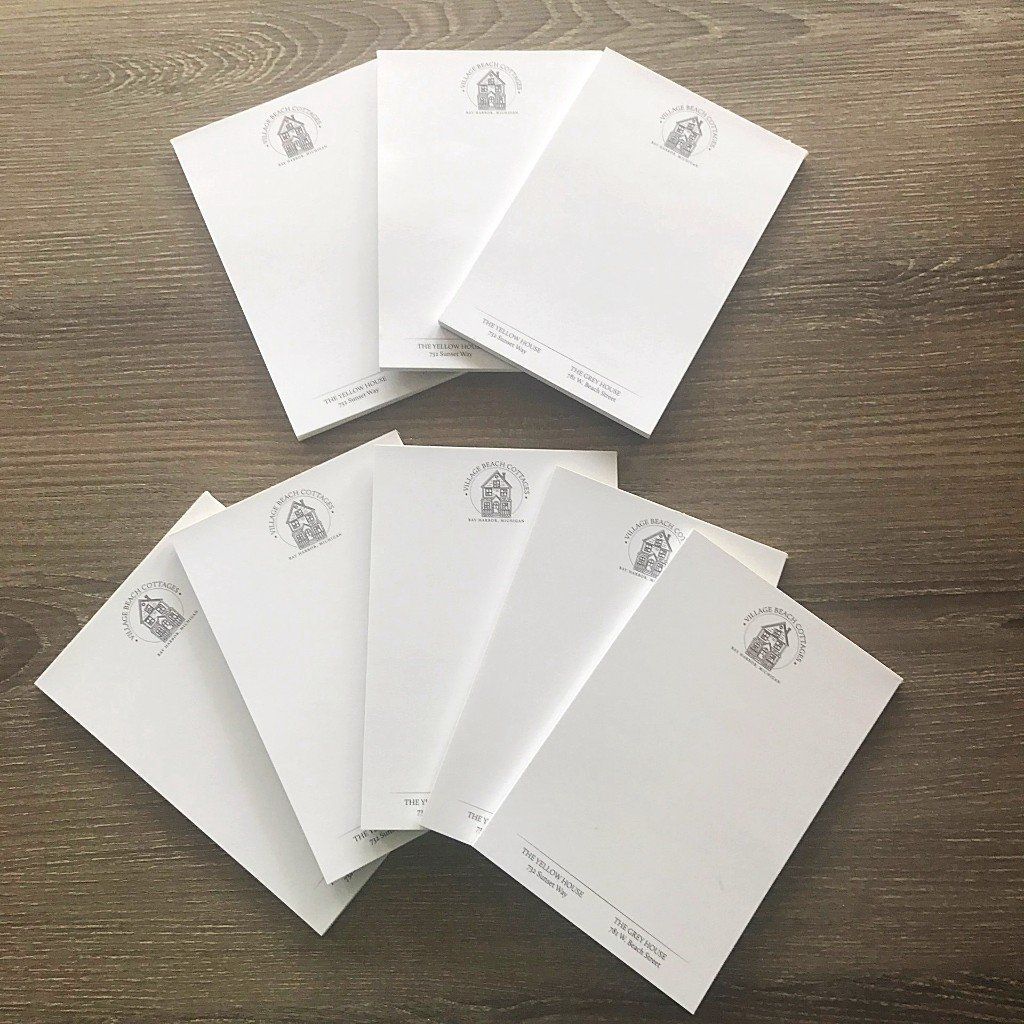 Seven white notepads arranged in two fan-shaped groups on a wooden table.