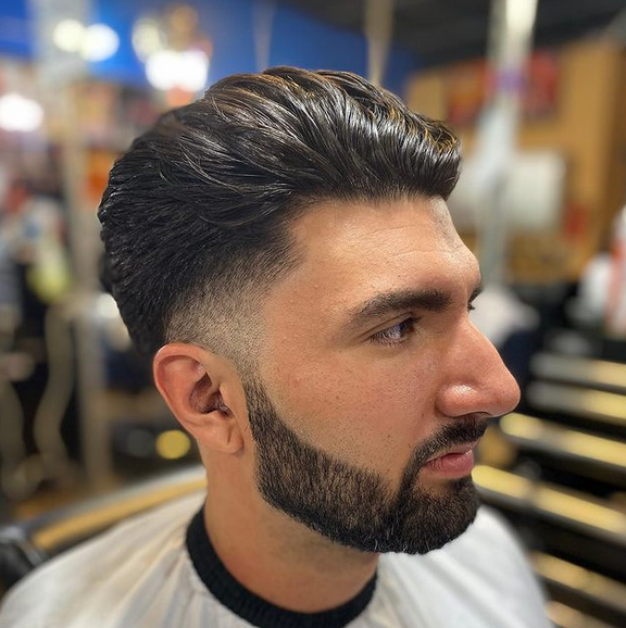 A man with a beard is getting his hair cut at a barber shop