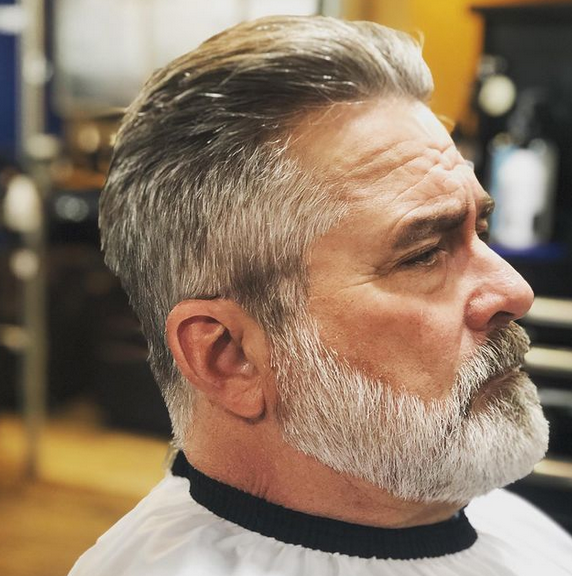 A man with a beard is getting his hair cut
