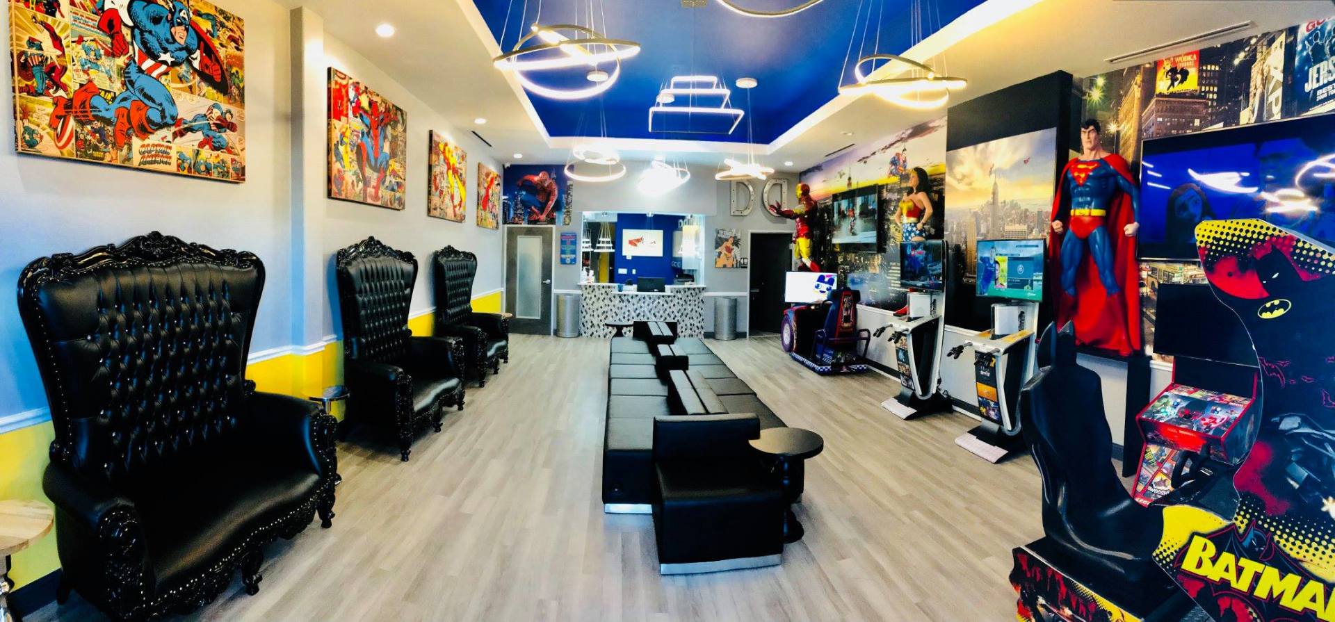 Bright comic-themed lounge with black chairs, low tables, blue ceiling lights, and Batman decor