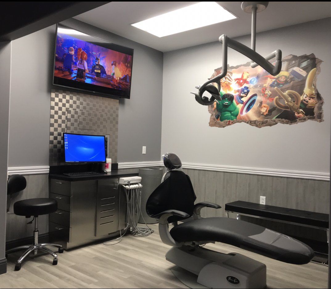 Modern clinic room with TV, computer desk, mural art, and an exam chair and table
