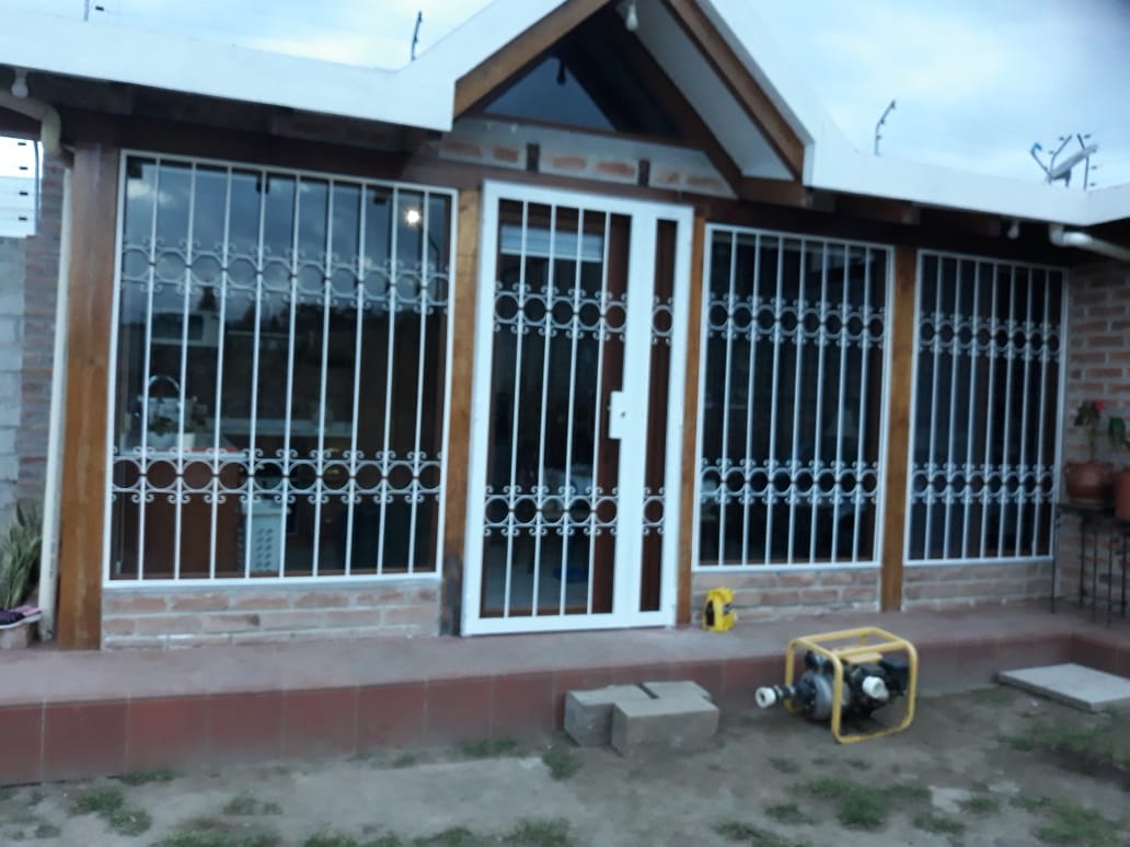 Una casa de una sola planta con una puerta con marco blanco y grandes ventanas cubiertas por rejas