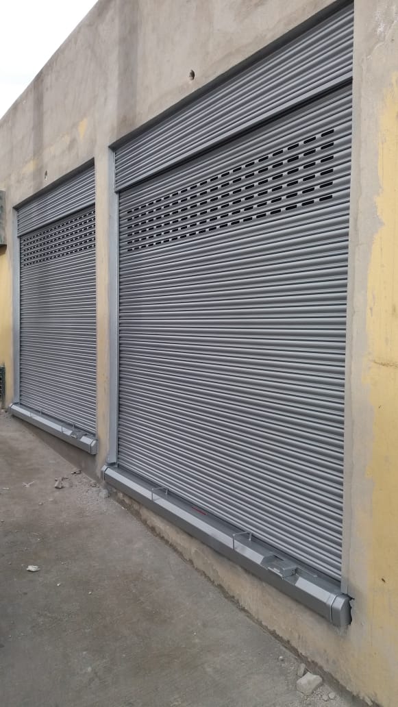 Dos persianas enrollables de metal gris que cubren las aberturas de ventanas o puertas en la fachada