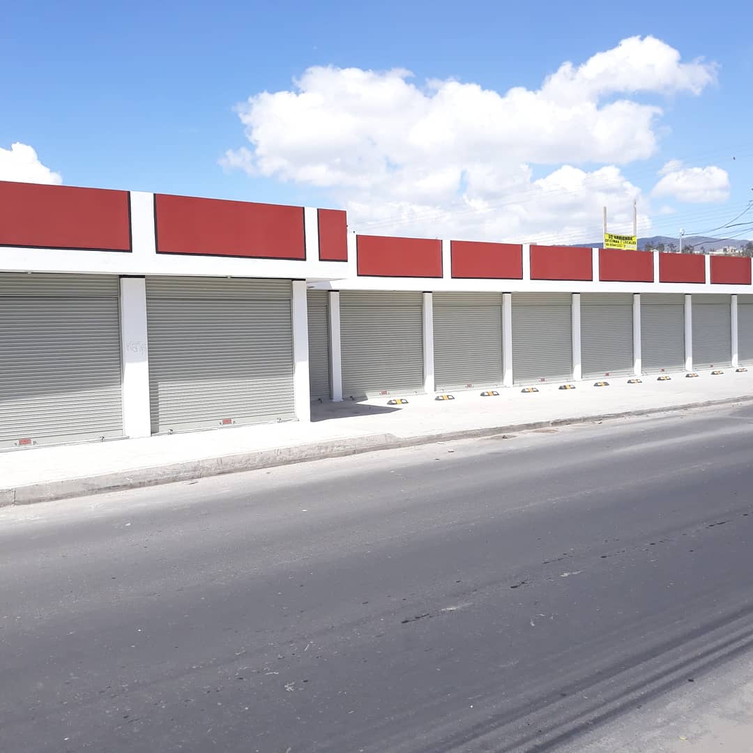 Una hilera de tiendas cerradas con contraventanas metálicas grises y fachada roja y blanc