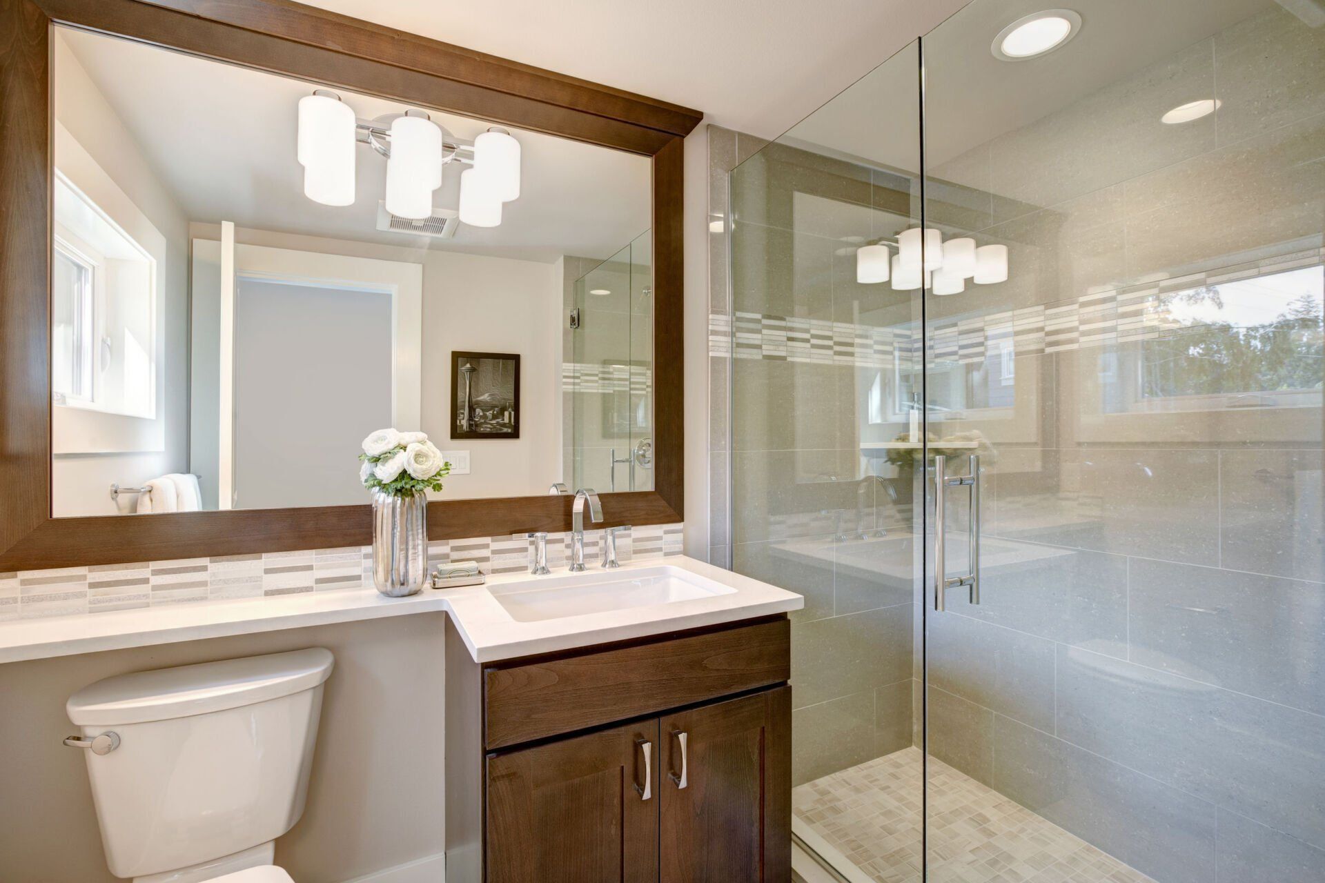 A bathroom with a toilet , sink , mirror and walk in shower.